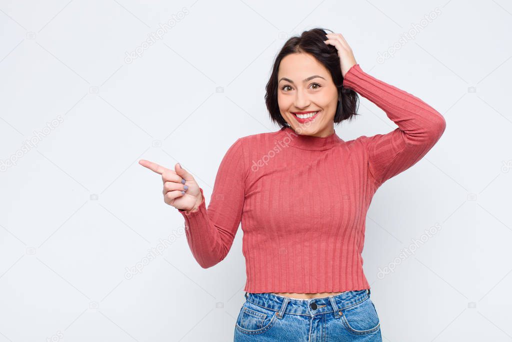 young pretty woman laughing, looking happy, positive and surprised, realizing a great idea pointing to lateral copy space against white wall