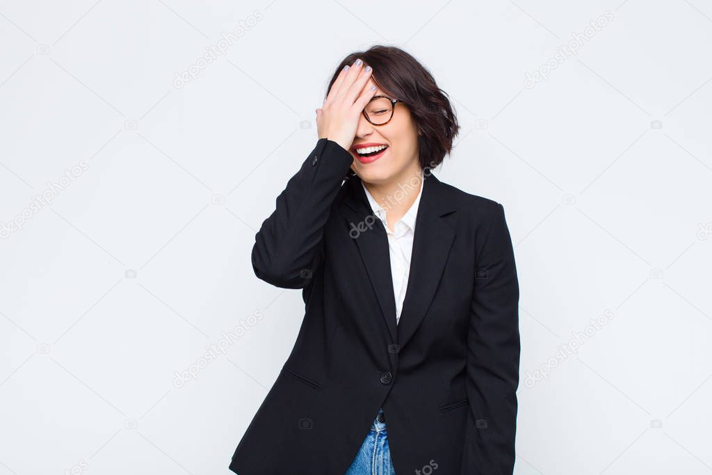 young businesswoman laughing and slapping forehead like saying doh! I forgot or that was stupid mistake against white wall