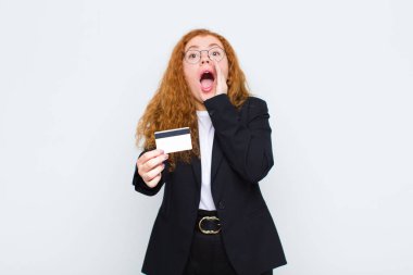 Kızıl saçlı genç kadın mutlu, heyecanlı ve pozitif hissediyordu. Elleri ağızda, beyaz duvara doğru bağırıyordu.