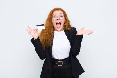 Kızıl saçlı genç kadın mutlu, heyecanlı, şaşırmış ya da şok olmuş hissediyor. Beyaz duvara karşı inanılmaz bir şeye gülümsüyor ve hayrete düşüyor.