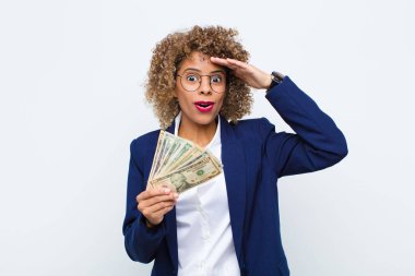 Genç Afrikalı Amerikalı kadın mutlu, şaşkın ve şaşırmış görünüyor, gülümsüyor ve avro banknotlarıyla inanılmaz ve inanılmaz iyi haberleri fark ediyor.