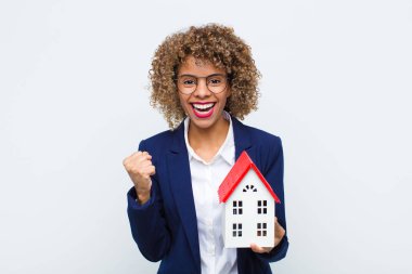 Genç Afrikalı Amerikalı kadın şok olmuş, heyecanlı ve mutlu hissediyor, gülüyor ve başarıyı kutluyor, vay canına! ev modeliyle