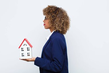 Profil görünümlü genç Afrikalı Amerikalı kadın ilerideki boşluğu kopyalamak istiyor. Düşünüyor, hayal ediyor ya da ev modeliyle hayal ediyor.