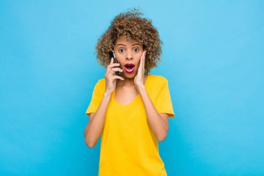 Genç Afro-Amerikan duyguları şok olmuş ve korkmuş görünüyor, ağzı açık ve elleri cep telefonuyla yanakları üzerinde.