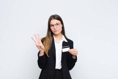 Genç, güzel bir kadın gülümsüyor ve arkadaş canlısı görünüyor. Üç ya da üç numarayı gösteriyor. Elleri önde, kredi kartıyla geri sayıyor.