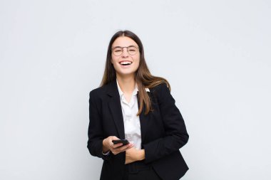Genç ve güzel bir kadın komik bir şakaya yüksek sesle gülüyor, mutlu ve neşeli hissediyor, cep telefonuyla eğleniyor.