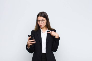 Genç ve güzel bir kadın ağzı açık, şok olmuş ve şaşırmış görünüyor. Cep telefonuyla kendini işaret ediyor.