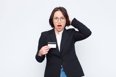 Genç, güzel bir kadın stresli, endişeli, endişeli ya da korkmuş, elleri başının üstünde, bir kredi kartıyla panikliyor.