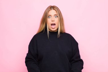 Genç sarışın kadın şok olmuş ya da şaşırmış görünüyor, ağzı açık bir şekilde düz duvara karşı 