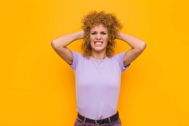 Genç afro kadın stresli, endişeli, endişeli ya da korkmuş hissediyor, elleri başının üstünde, turuncu duvara karşı panikliyor.