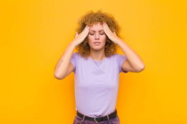 Genç afro kadın konsantre, düşünceli ve ilham verici görünüyor, beyin fırtınası yapıyor ve elleri turuncu duvarda hayal ediyor.