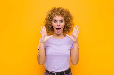 Turuncu duvara karşı inanılmaz bir şey fark ettiğinde genç afro kadın şaşırmış ve şaşkın bakıyordu.