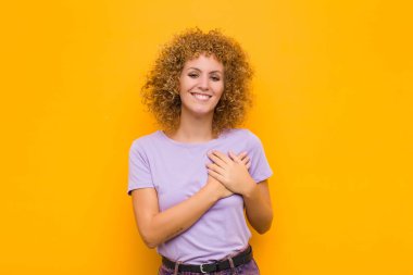 Genç afro kadın romantik, mutlu ve aşık, neşeli bir şekilde gülümsüyor ve turuncu duvarın karşısında el ele tutuşuyor.