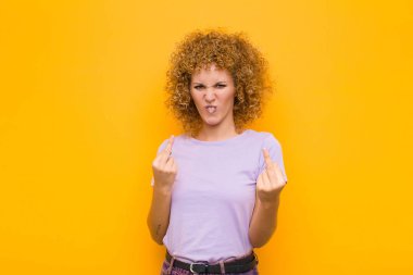 Genç afro kadın kışkırtıcı, agresif ve müstehcen hissediyor, orta parmağı çeviriyor, turuncu duvara karşı isyankar bir tavır sergiliyor.