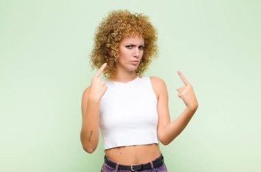 Kötü tavırlı genç afro kadın gururlu ve agresif görünüyor, yukarı bakıyor ya da yeşil duvara yaslanmış ellerle dalga geçiyor.