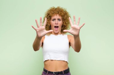 Genç afro kadın sersemlemiş ve korkmuş hissediyor, korkunç bir şeyden korkuyor, elleri açık yeşil duvardan uzak durun diyor.