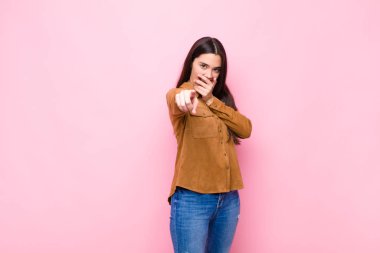 Genç ve güzel bir kadın sana gülüyor, kamerayı işaret ediyor ve seninle dalga geçiyor ya da pembe duvara karşı alay ediyor.