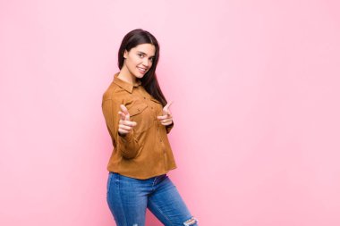 Genç, güzel bir kadın kendini mutlu, havalı, tatmin olmuş, rahat ve başarılı hissediyor, kameraya bakıyor, pembe duvara karşı seni seçiyor.