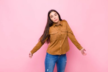 Genç, güzel bir kadın kendini cahil ve şaşkın hissediyor. Hiçbir fikri yok. Pembe duvara karşı aptal ya da aptal bir bakışla kafası karışmış.