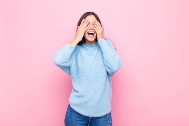 Genç ve güzel bir kadın gülümsüyor ve mutlu hissediyor, iki eliyle gözlerini kapatıyor ve pembe duvara karşı inanılmaz bir sürpriz bekliyor.