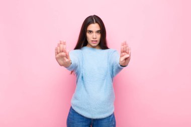 Genç ve güzel bir kadın ciddi, mutsuz, kızgın ve hoşnutsuz görünüyor. Ya da her iki avucunuzu pembe duvara dayayıp durun diyor.