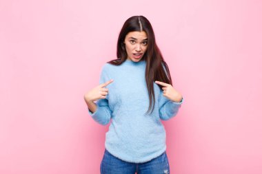 Genç, güzel bir kadın kendini mutlu, şaşırmış ve gururlu hissediyor. Heyecanlı ve şaşkın bir şekilde pembe duvara bakıyor.