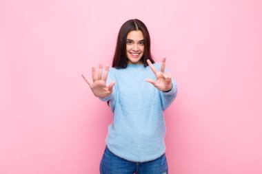 Genç, güzel bir kadın gülümsüyor ve arkadaş canlısı görünüyor. 8 ya da 8 numarayı gösteriyor. Elleri önde, pembe duvara doğru sayıyor.