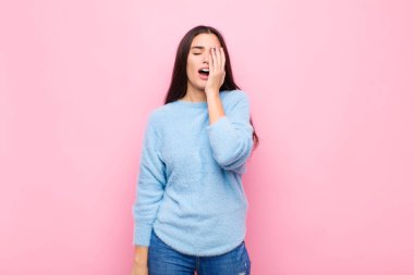 Genç ve güzel bir kadın uykulu görünüyor, sıkılmış ve esniyor, baş ağrısı ve yüzünün yarısını pembe duvarla kaplıyor.