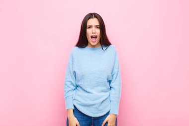 Genç ve güzel bir kadın agresif bir şekilde bağırıyor. Kızgın, sinirli, öfkeli ya da sinirli görünüyor. Pembe duvara karşı hayır diye bağırıyor.