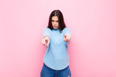 Genç ve güzel bir kadın kameraya iki parmağını ve kızgın bir ifadeyle bakıyor ve sana pembe duvara karşı görevini yapmanı söylüyor.