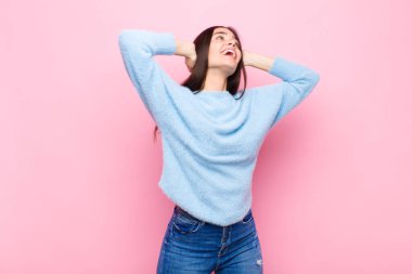 Genç ve güzel bir kadın gülümsüyor ve rahatlıyor, tatmin oluyor ve kaygısız, pozitif gülüyor ve pembe duvara karşı ürperiyor.