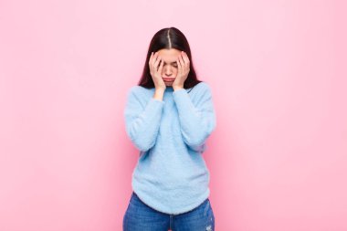 Genç ve güzel bir kadın stresli ve hayal kırıklığına uğramış görünüyor. Baskı altında çalışıyor ve pembe duvara karşı sorunlarla boğuşuyor.