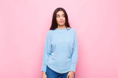 Genç, güzel bir kadın, merak ediyor, mutlu düşünceler ve fikirler düşünüyor, hayal kuruyor, pembe duvara karşı uzayı kopyalamaya çalışıyor.