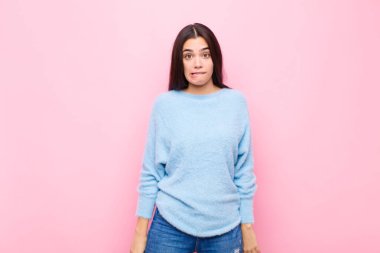 Genç ve güzel bir kadın şaşkın ve şaşkın görünüyor, gergin bir jestle dudaklarını ısırıyor, pembe duvara karşı sorunun cevabını bilmiyor.