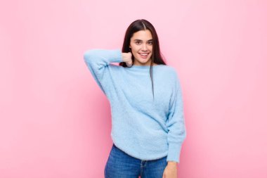 Genç, güzel bir kadın, pembe duvarın karşısında neşeli ve kendinden emin bir şekilde gülüyor.