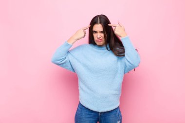 Ciddi ve konsantre bakışları olan genç ve güzel bir kadın pembe duvara karşı zorlu bir sorun düşünüyor ve beyin fırtınası yapıyor.