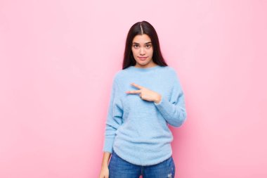 Genç, güzel bir kadın kendini mutlu, pozitif ve başarılı hissediyor. Göğsünde V şeklinde eller yapıyor. Pembe duvara karşı zafer ya da barış gösteriyor.