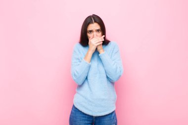Genç ve güzel bir kadın elleri ile ağzını kapatıyor, şok olmuş, şaşırmış bir ifadeyle, bir sır saklıyor veya pembe duvara karşı 