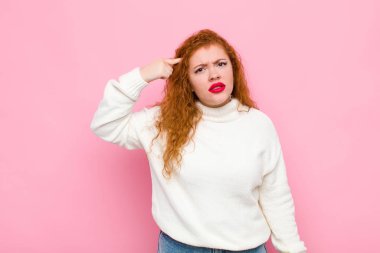 Genç kızıl saçlı kadın şaşkın ve şaşkın hissediyor. Deli, deli ya da pembe duvara karşı aklını kaçırmış olduğunu gösteriyor.