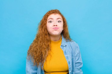 Aptal, çılgın, şaşkın bir ifadeyle genç kızıl saçlı kadın. Yanakları şişmiş, içi doldurulmuş, şişman ve mavi duvarda yemek dolu.