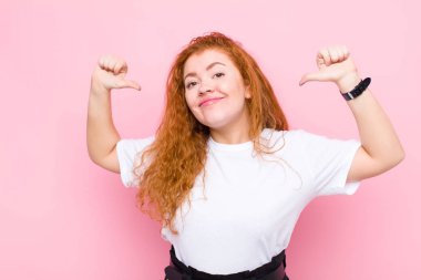 Genç kızıl saçlı kadın gururlu, kibirli ve kendinden emin görünüyor. Tatmin olmuş ve başarılı görünüyor. Kendini pembe duvara gösteriyor.