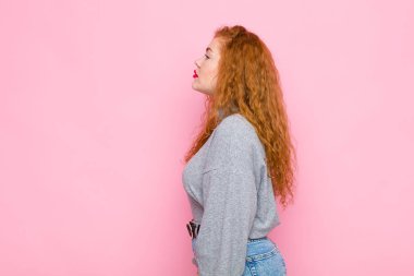 Profil görünümlü genç kızıl saçlı kadın uzayı kopyalamaya çalışıyor, düşünüyor, hayal ediyor ya da pembe duvara karşı hayal kuruyor.