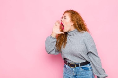 Genç kızıl saçlı kadın öfkeyle bağırıyor kenardaki boşluğu kopyalamak için, eli ağzının yanında pembe duvara yaslanmış.