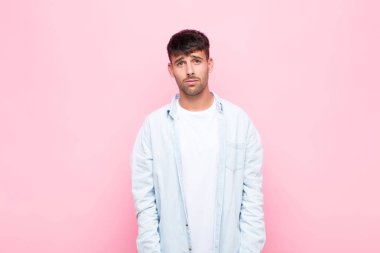 Genç yakışıklı adam üzgün ve stresli. Kötü bir sürpriz yüzünden üzgün. Pembe duvara karşı olumsuz ve endişeli bir bakışla bakıyor.