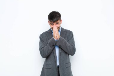 Genç yakışıklı adam mutlu, neşeli, şanslı ve şaşırmış görünüyor. İki eli de beyaz duvara dayalı.