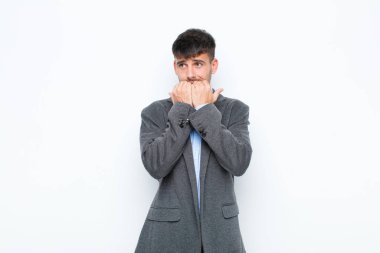 Genç yakışıklı adam endişeli, endişeli, stresli ve korkmuş görünüyor, tırnaklarını yiyor ve beyaz duvara karşı yanal fotokopi alanı arıyor.