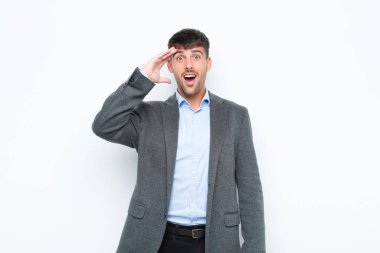 Genç yakışıklı adam mutlu, şaşkın ve şaşırmış görünüyor, gülümsüyor ve beyaz duvara karşı inanılmaz ve inanılmaz iyi haberler veriyor.