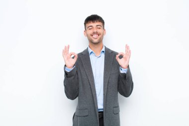 Genç yakışıklı adam konsantre olmuş ve meditasyon yapıyor, tatmin olmuş ve rahatlamış hissediyor, düşünüyor ya da beyaz duvara karşı bir seçim yapıyor.