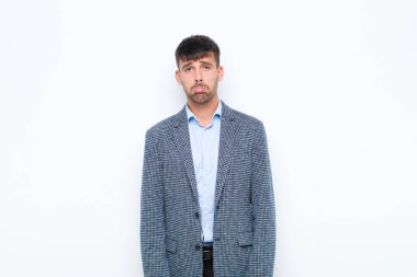Genç yakışıklı adam üzgün ve stresli. Kötü bir sürpriz yüzünden üzgün. Beyaz duvara karşı olumsuz ve endişeli bir bakışla bakıyor.