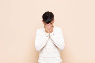 Genç yakışıklı adam üzgün, hayal kırıklığına uğramış, gergin ve depresif, iki eliyle yüzünü kapatıyor, sıcak duvara karşı ağlıyor.